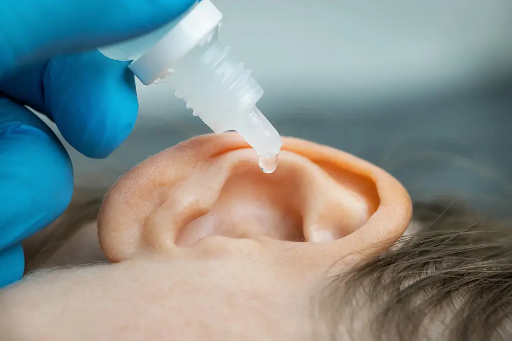 A person dripping a drop of liquid into a ear.