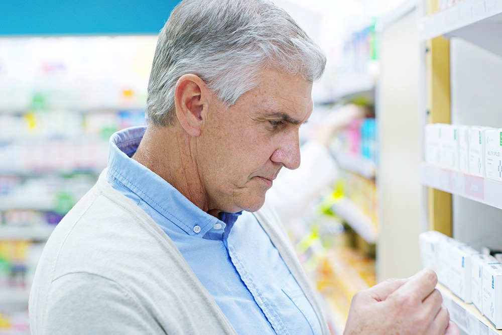 An older man with gray hair is standing in a pharmacy aisle.