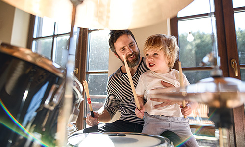 Small boy with father indoors at home, playing drums.